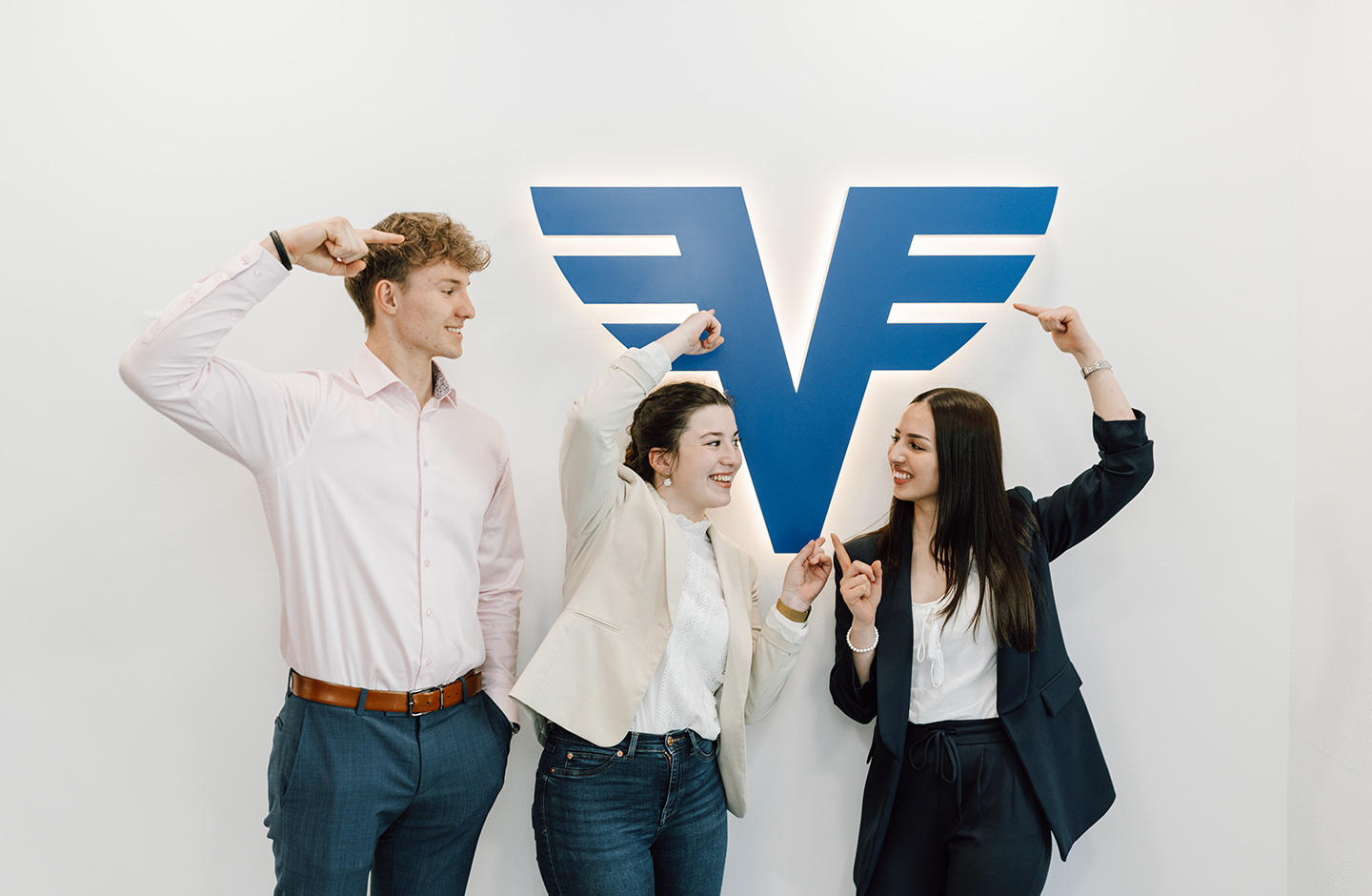 Drei Mitarbeiter zeigen auf unser Volksbank-Logo an der Wand