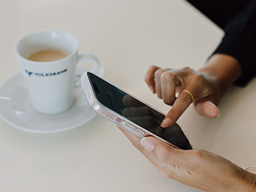 Handy in der Hand und Kaffeetasse daneben