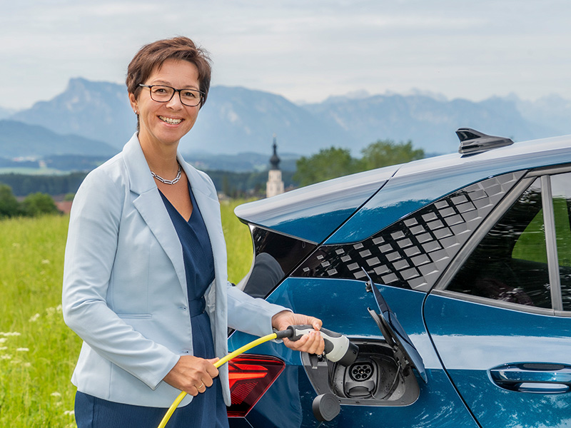 Mitarbeiterin steht neben E-Auto und lacht