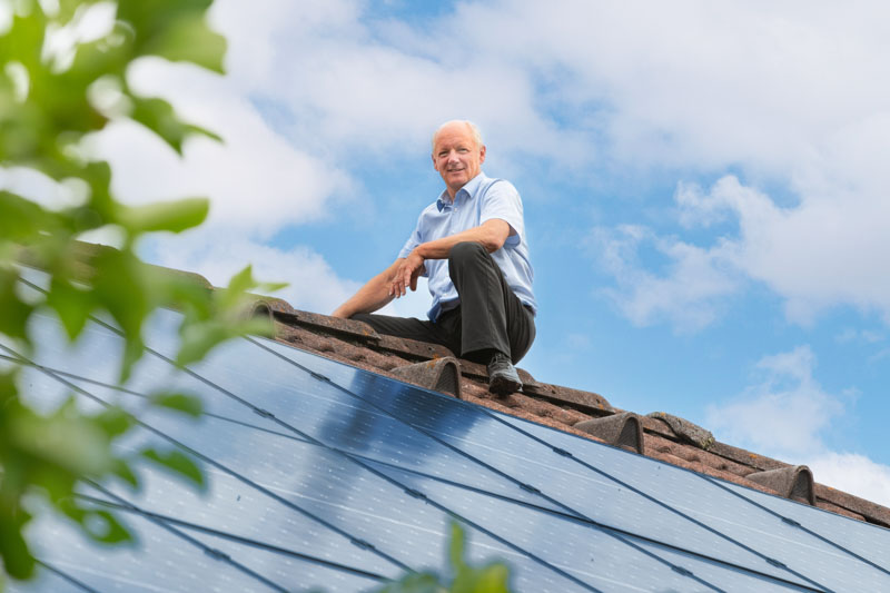 Mitarbeiter sitzt am Dach neben seiner Photovoltaikanlage