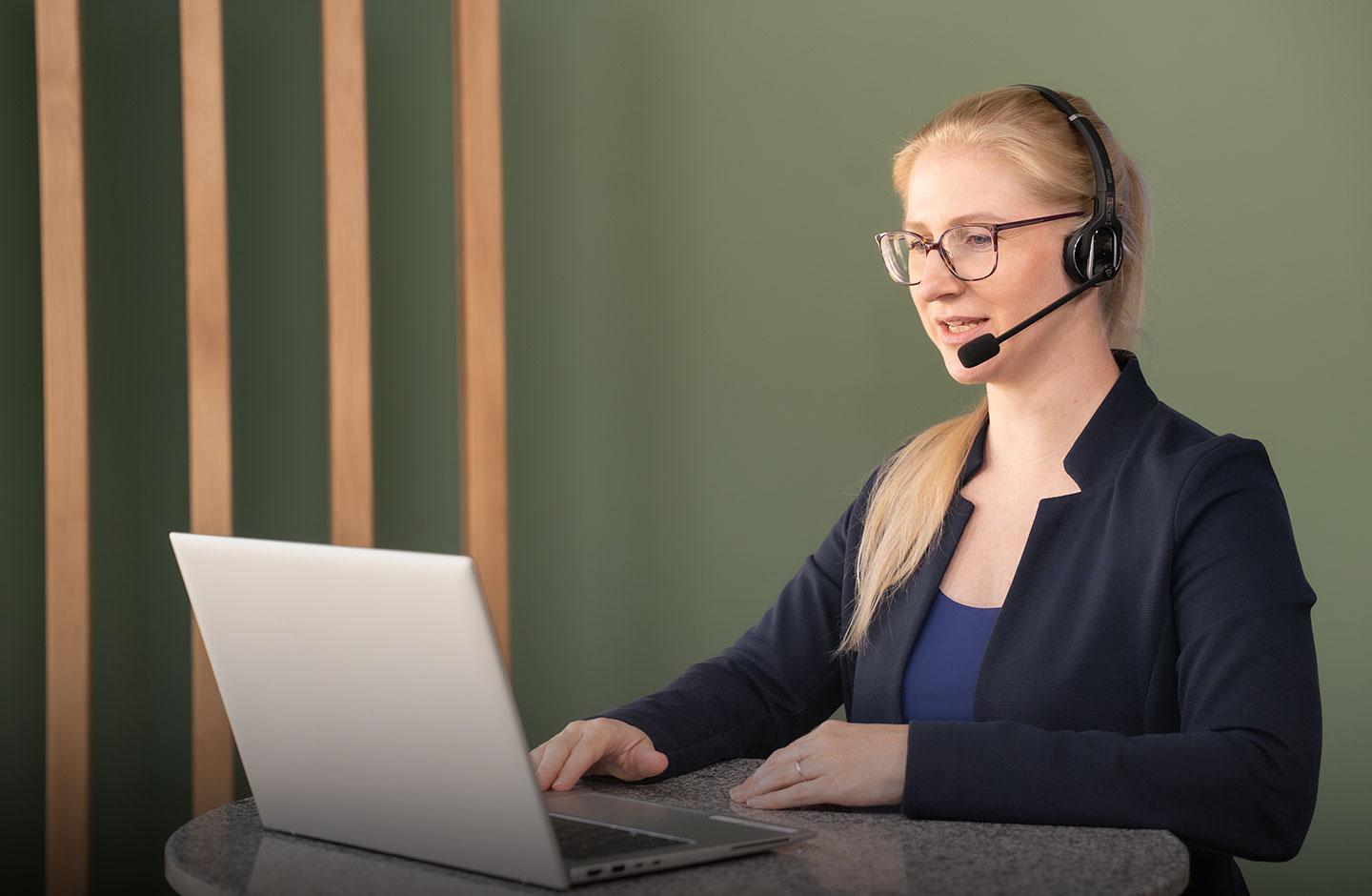 Eine Frau an einem Tisch stehend mit einem Headset und einem Laptop