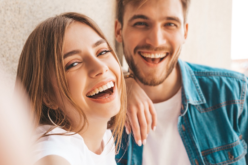 Ein junges Paar macht ein Selfie. Die Frau hält die Kamera, beide lachen.