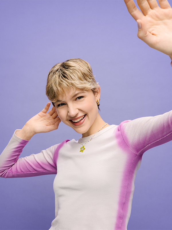 Junge Dame mit kurzen blonden Haaren posiert vor lila Hintergrund