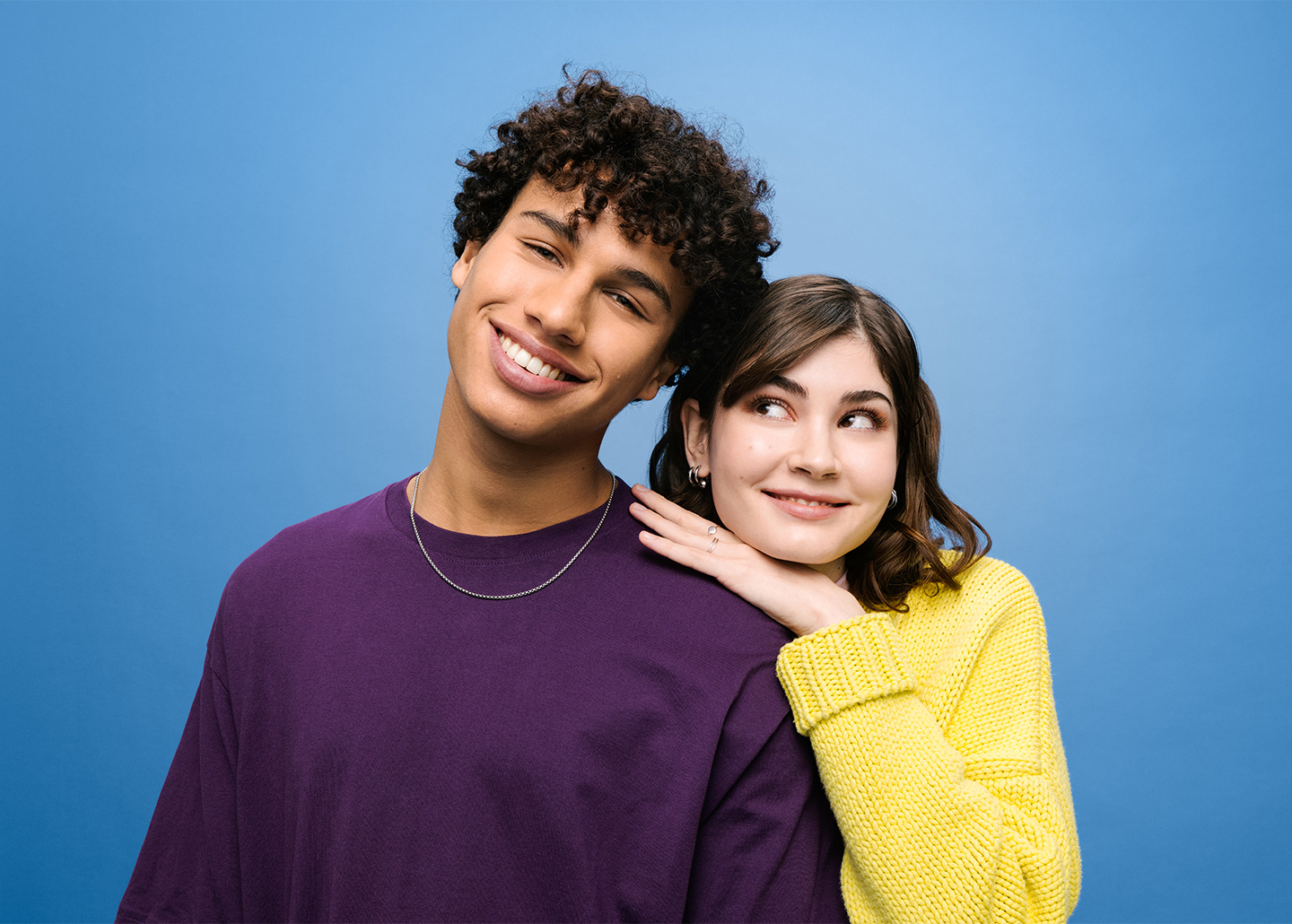 Zwei Freunde, ein Junge und ein Mädchen lachen vor blauem Hintergrund in die Kamera.