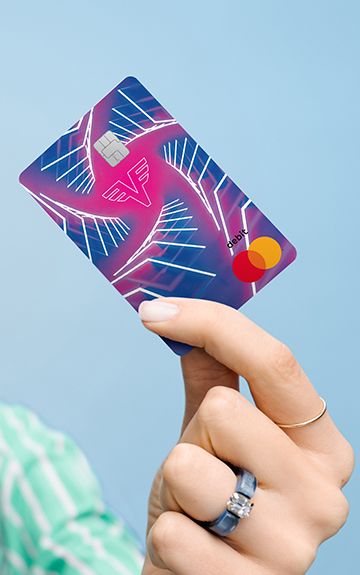 Eine junge Frau Mann mit blonden, kurzen Haaren hält lächelnd eine Debit Mastercard der Volksbank in der Hand.