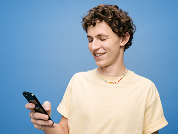 Ein junger Mann mit gelockten Haaren schaut auf sein Mobiltelefon.
