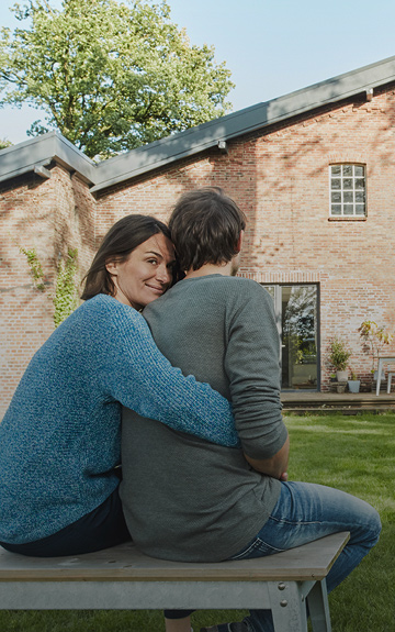 Frau und Mann umarmen sich vor ihrem Eigenheim