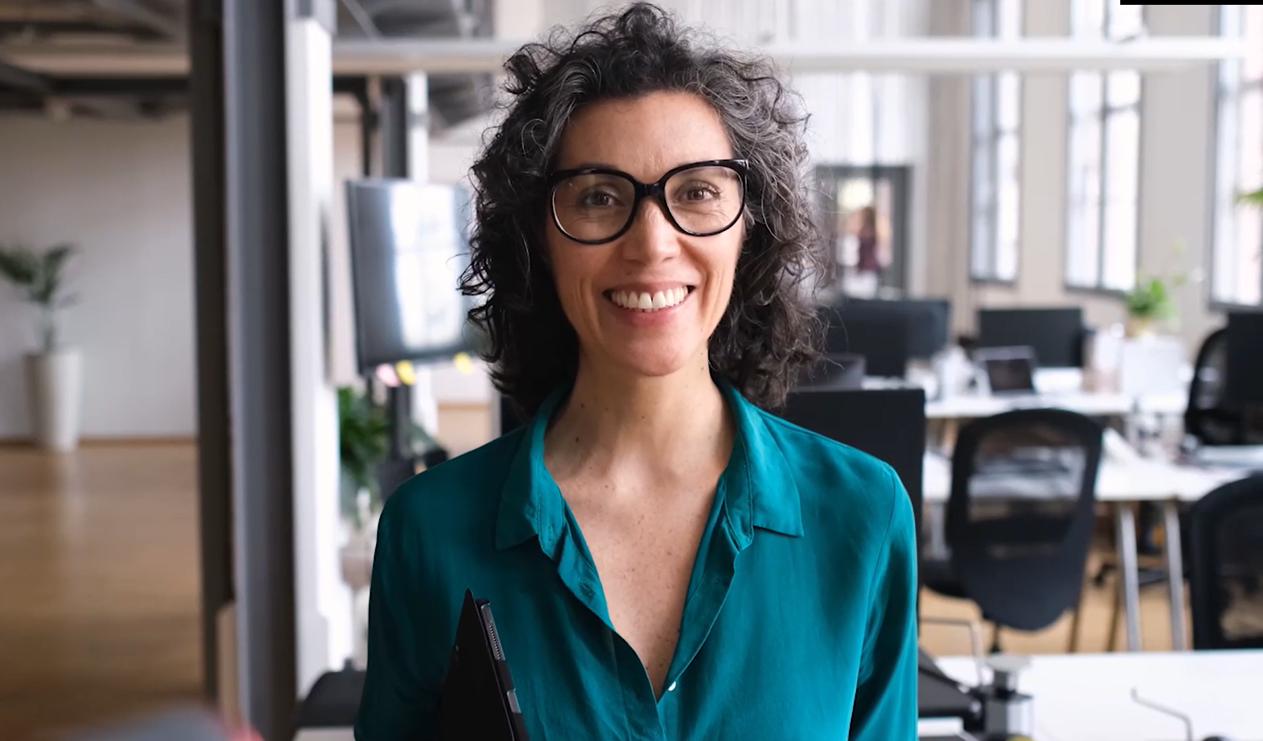 Eine Frau mit lockigem, dunklen Haar und Brille grinst.