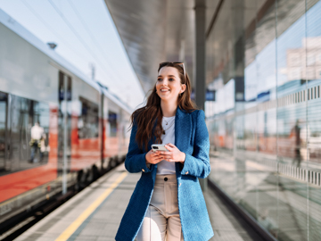 Eine Frau geht auf dem Bahnsteig. Sie hat ein Mobiltelefon in der Hand.