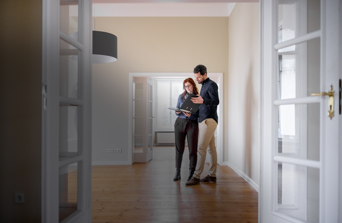 Ein Pärchen steht in einer leeren Wohnung und betrachtet Pläne in einem Ordner.